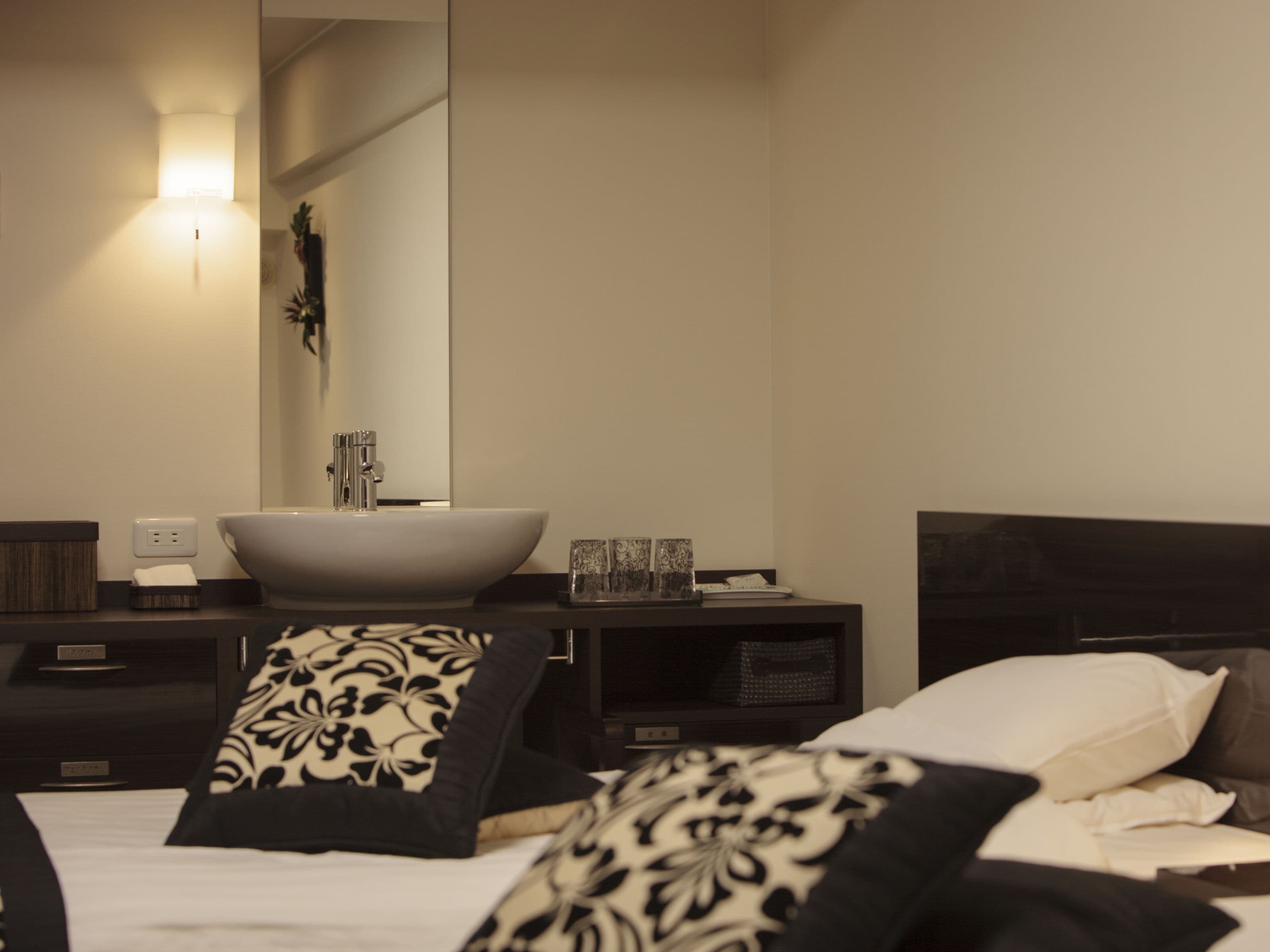 A modern bedroom with a large bed, a bedside table with a white basin, and a mirror above the sink.