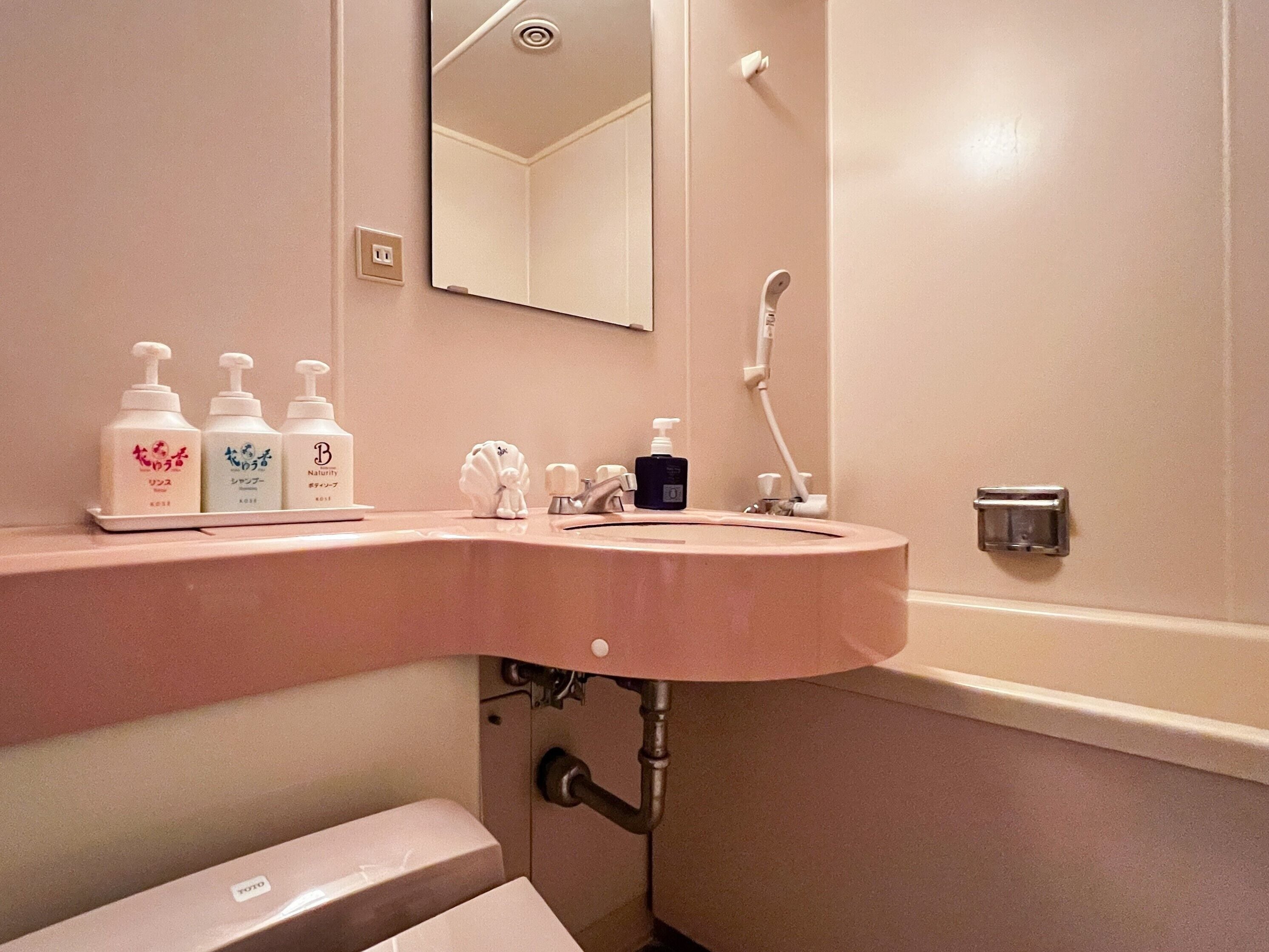 A bathroom with a pink sink, a mirror, and three bottles of toiletries on the counter.