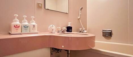 A bathroom with a pink sink, a mirror, and three bottles of toiletries on the counter.