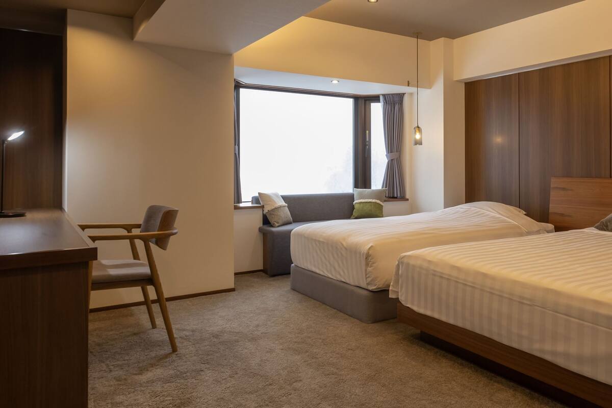 Une chambre d’hôtel équipée d’un bureau, de deux lits, d’une fenêtre avec des rideaux et offrant une vue sur l’extérieur.