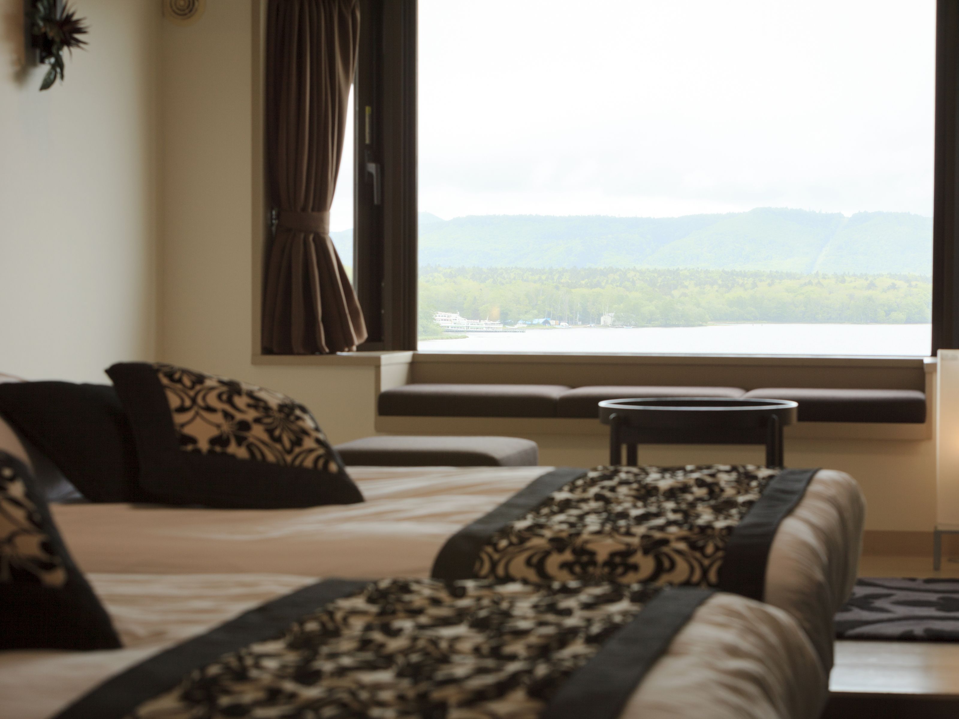 Une chambre d’hôtel avec deux lits, une fenêtre donnant sur les montagnes et une petite table.