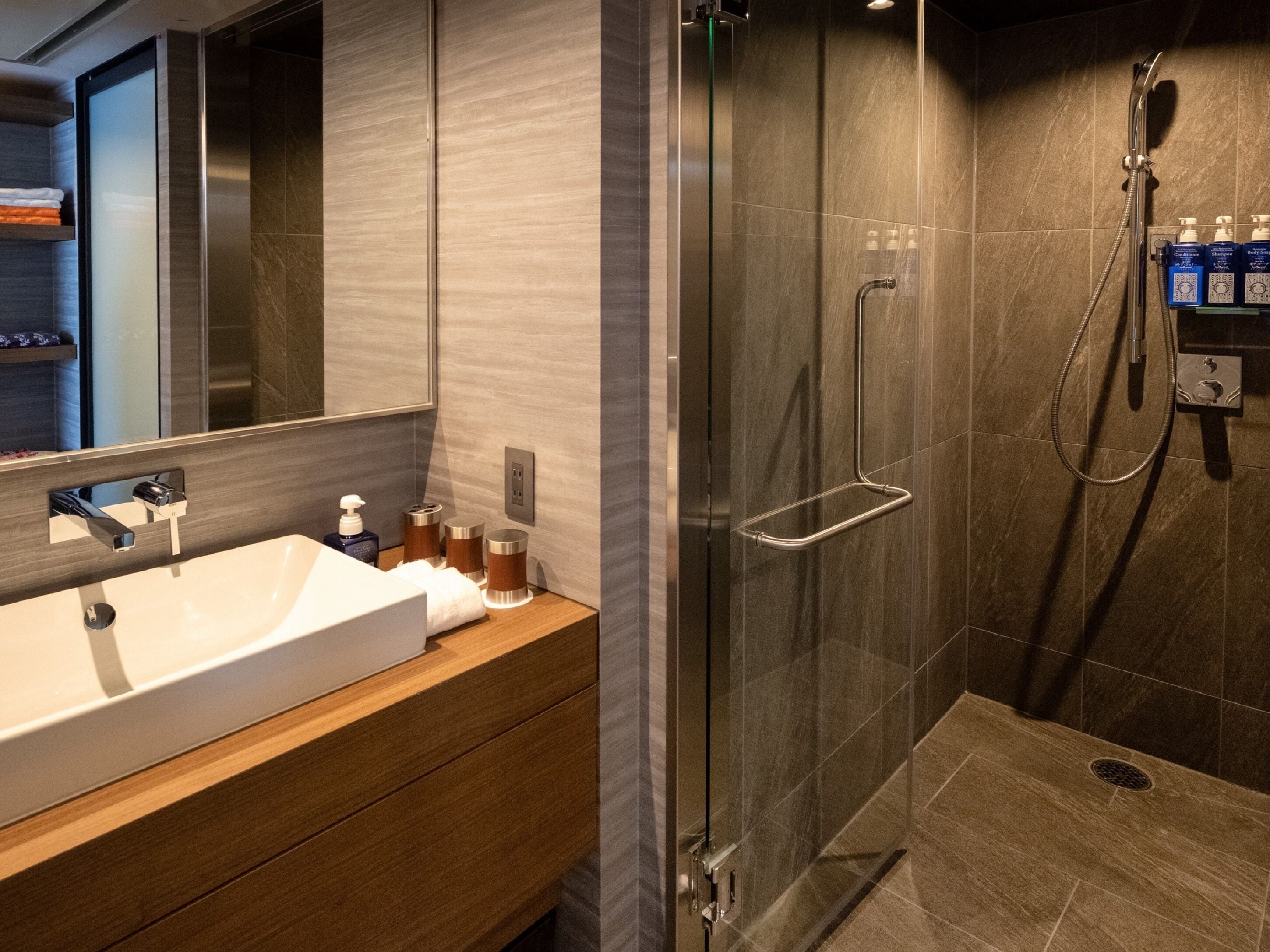 A modern bathroom with a glass-enclosed shower, a white sink, and a wooden vanity.