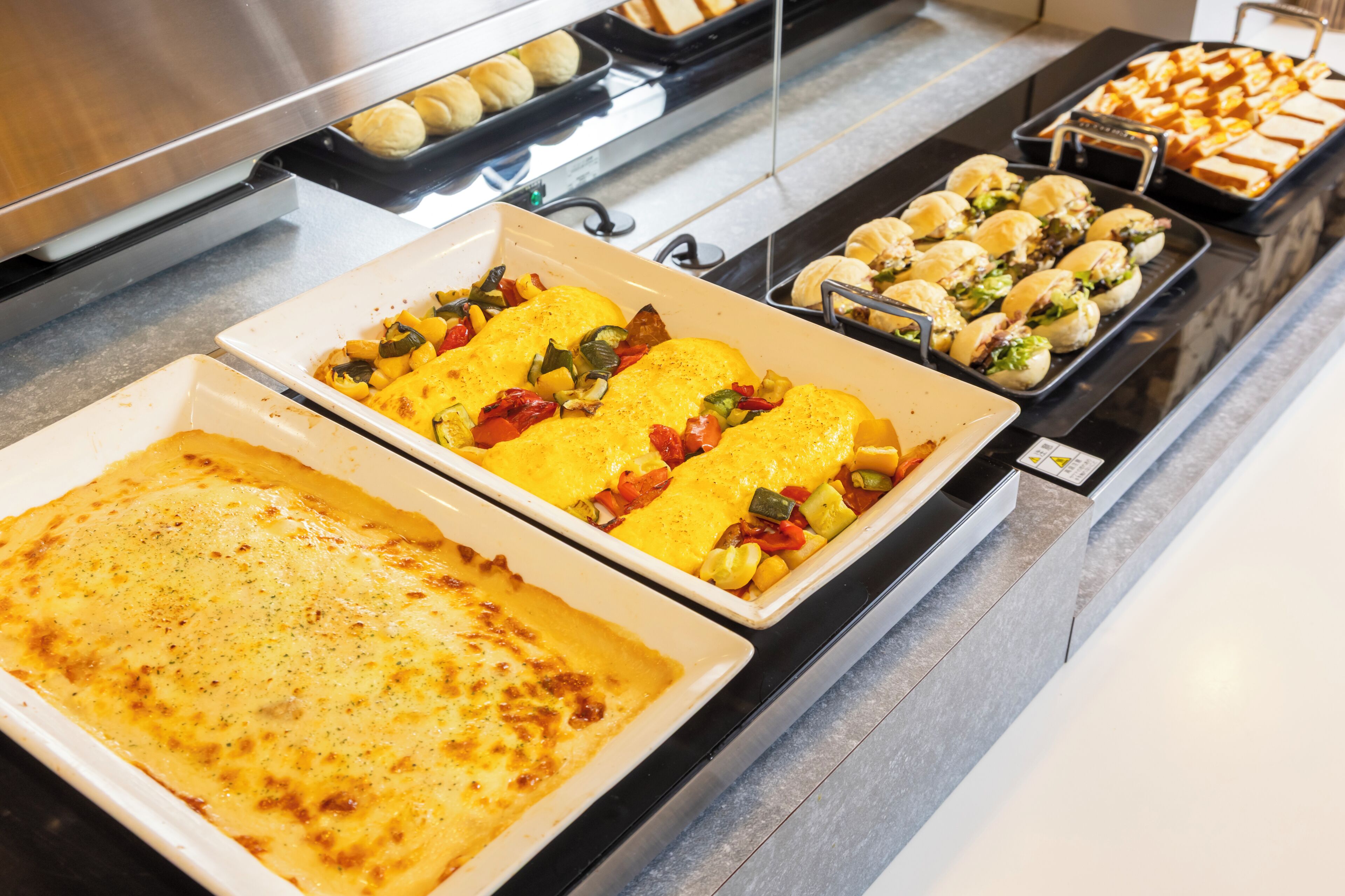 Un bufé con diversos platos, incluyendo un pastel de carne, verduras rellenas y sándwiches.