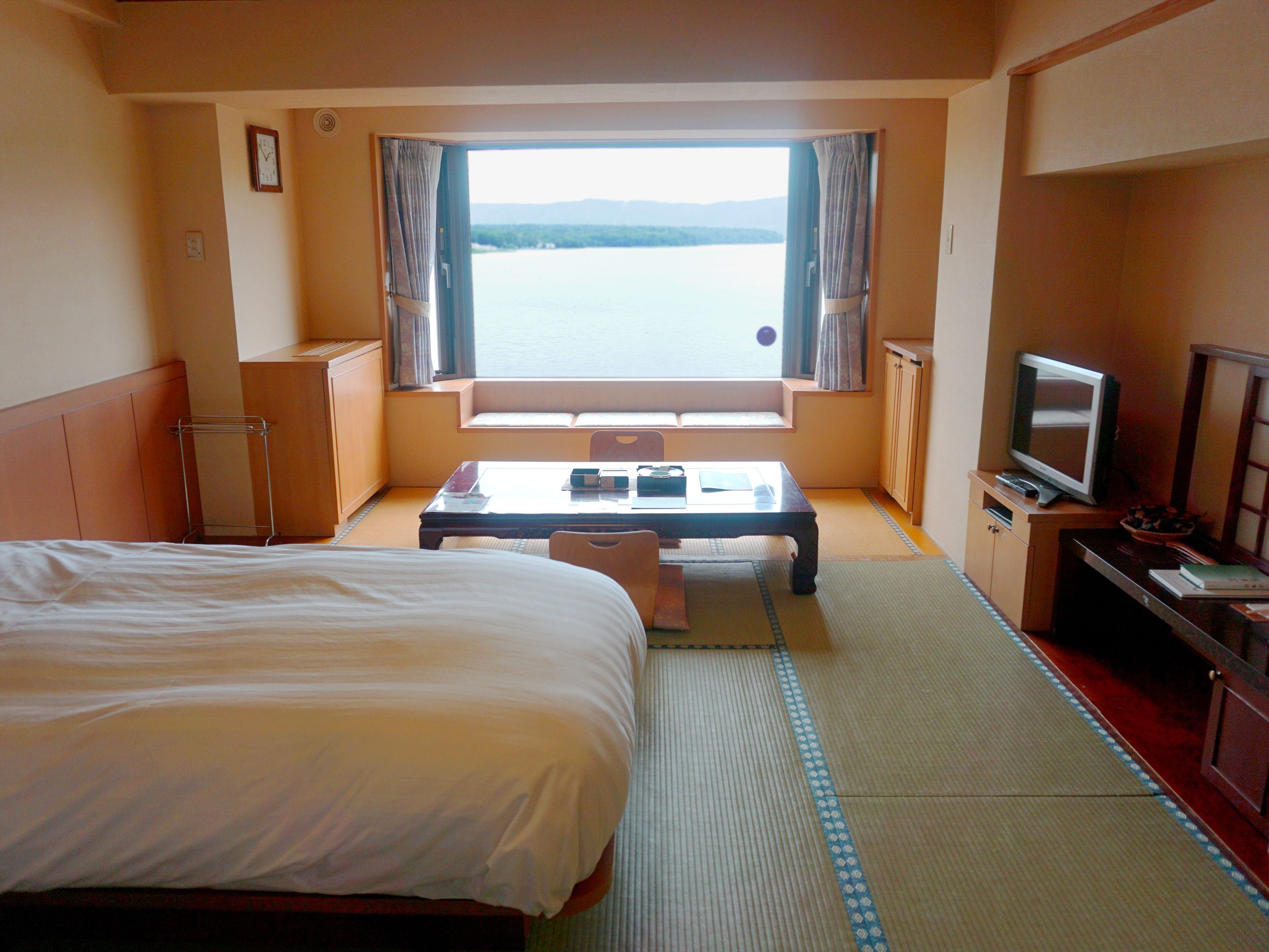 A hotel room with a bed, a small table, a television, and a view of the water.