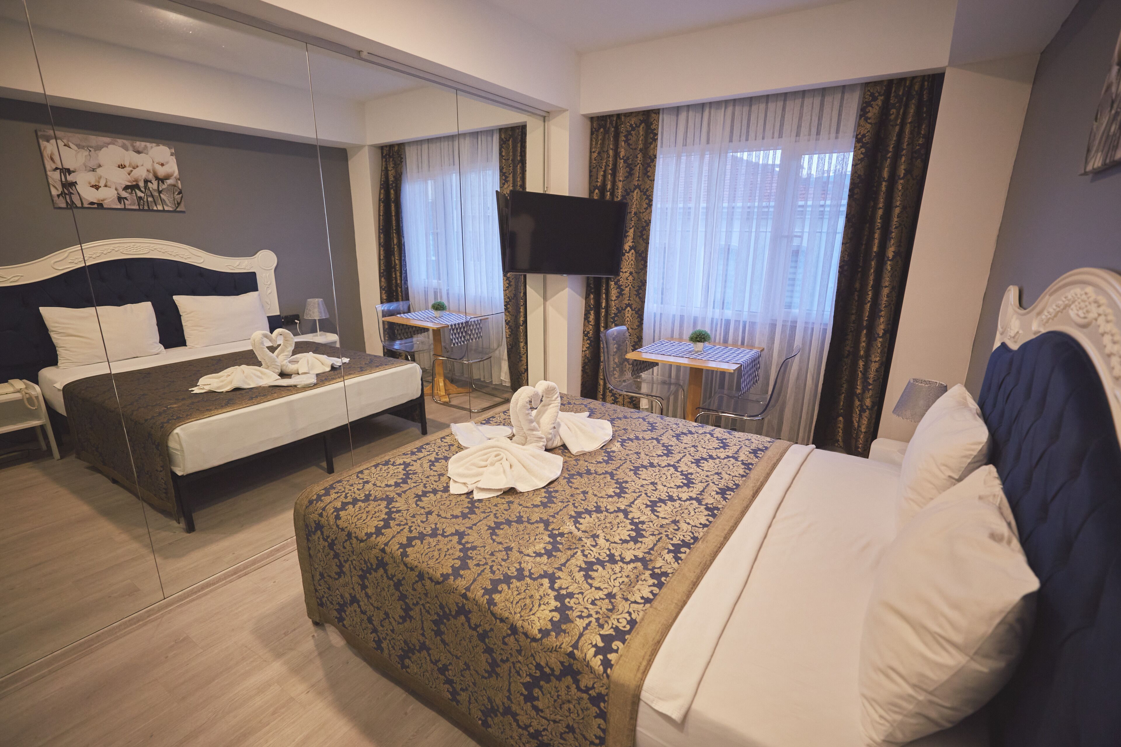 A hotel room with a large bed, a smaller bed, a desk with a chair, a TV, and a window with curtains.