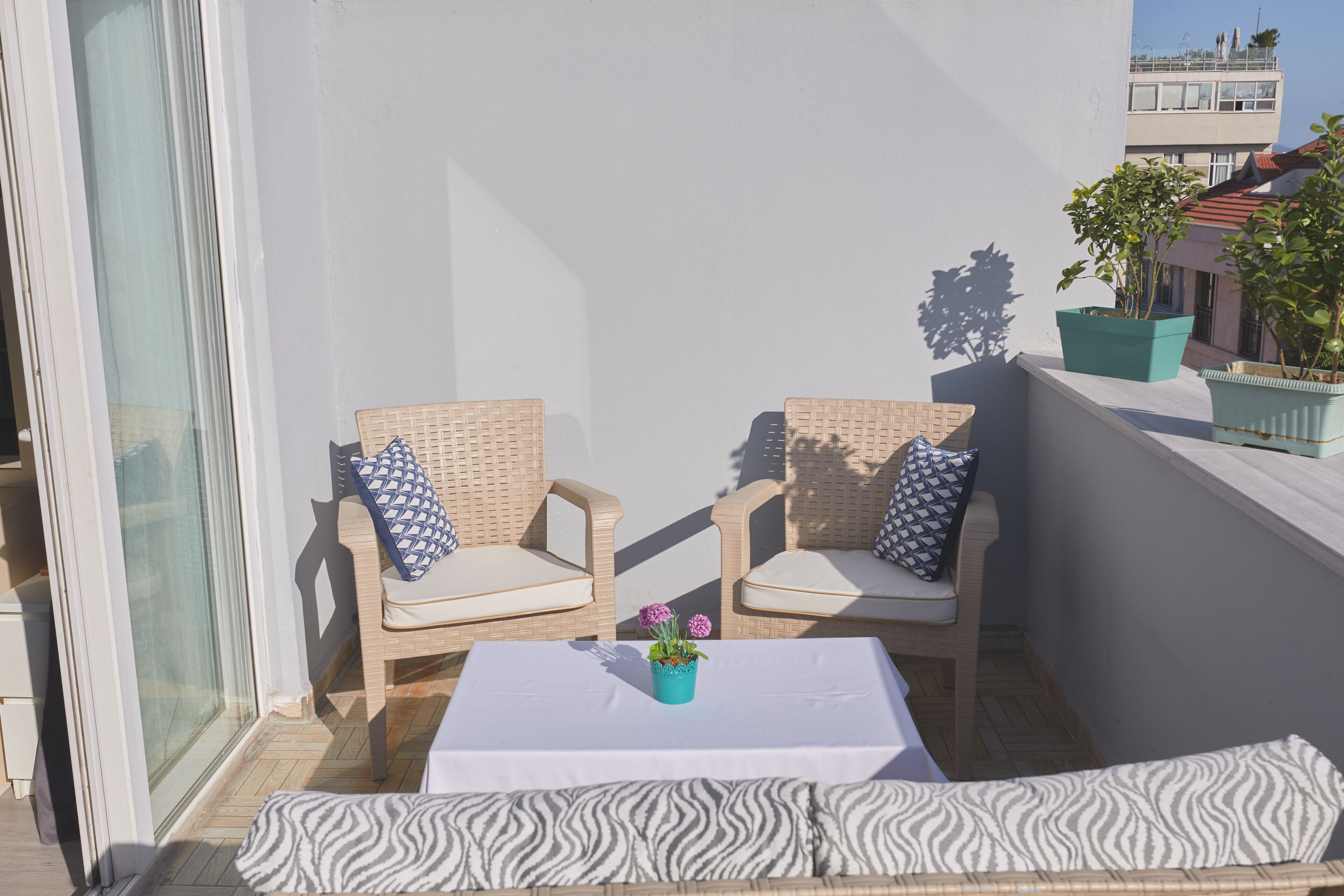 Een balkon met rieten stoelen, een klein tafeltje en een potplant.