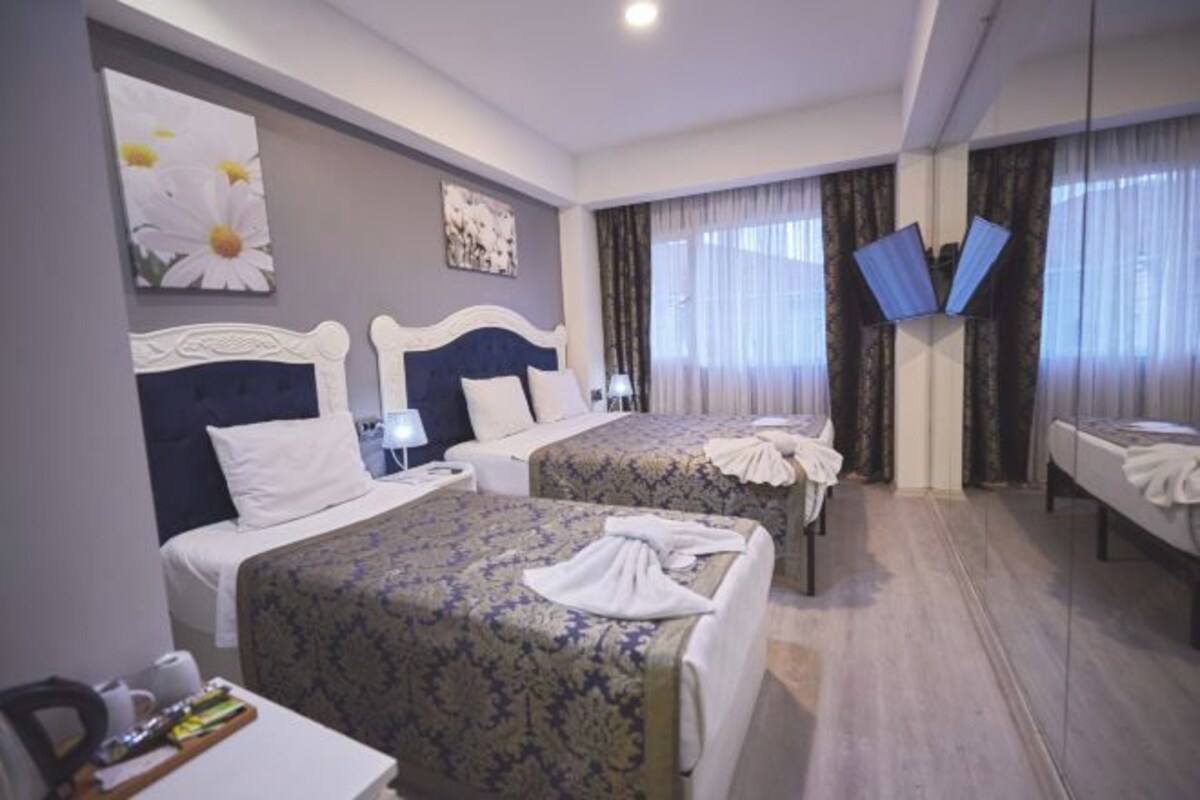 Une chambre d’hôtel avec deux lits, un téléviseur à écran plat, une table de chevet et une fenêtre avec des rideaux.