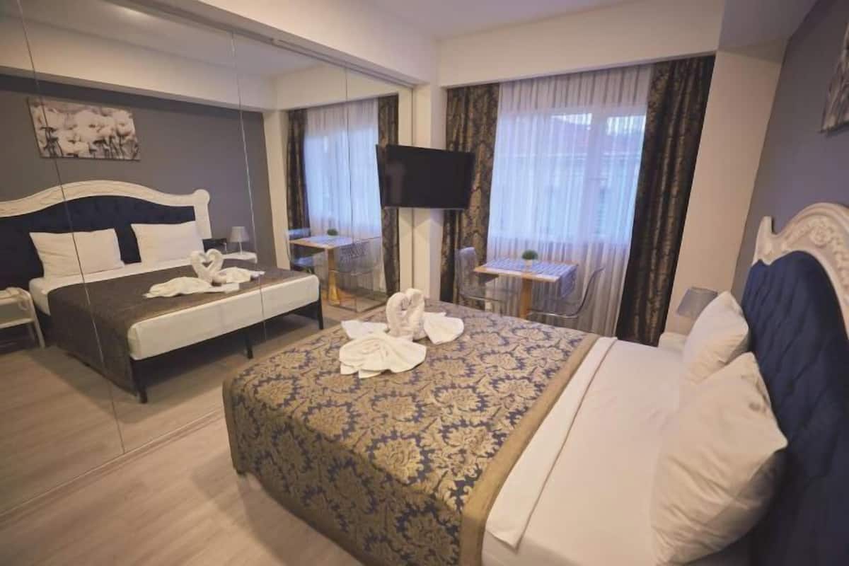 Ein Hotelzimmer mit einem großen Bett, einem Schreibtisch mit Stuhl, einem Fernseher und einem Fenster mit Vorhängen.