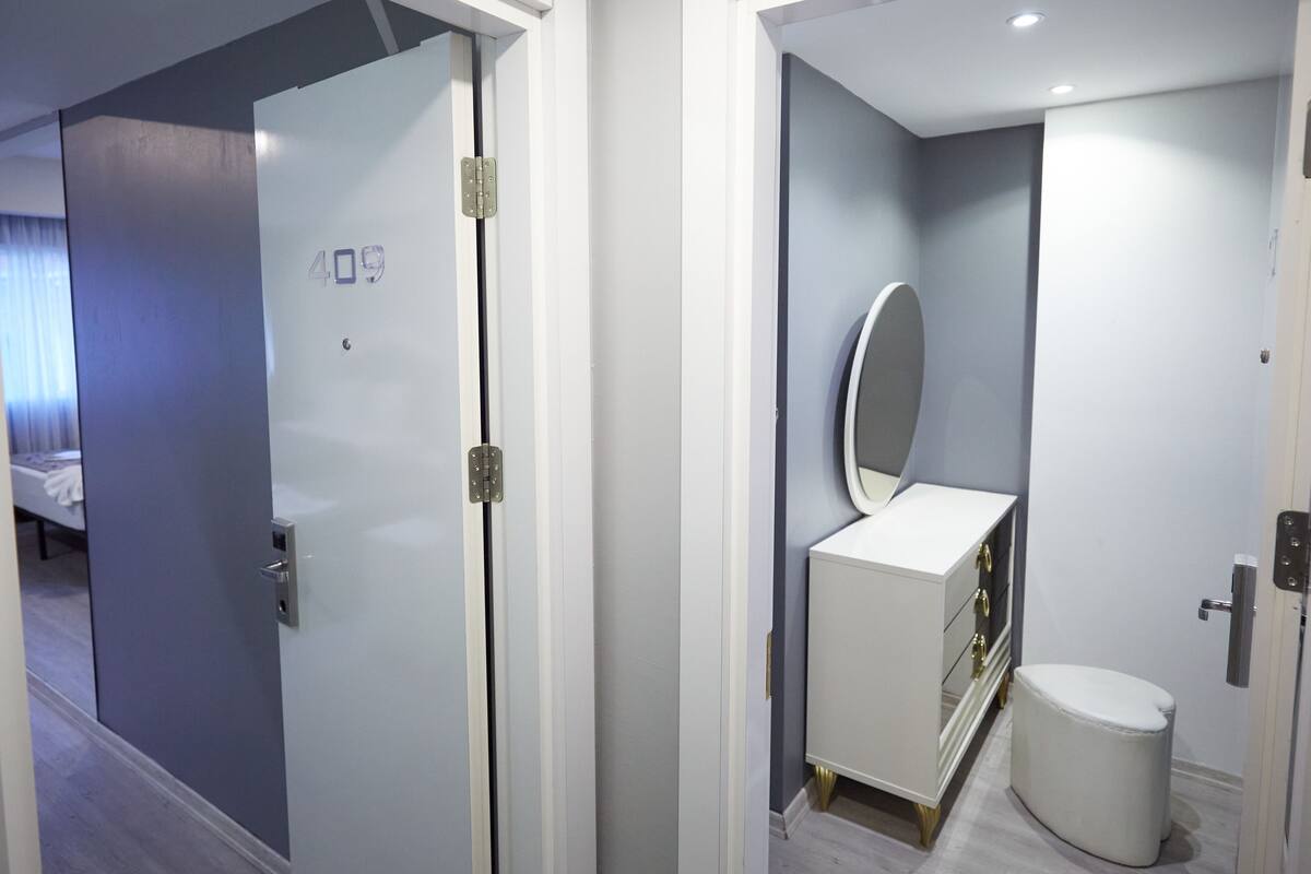Ein modernes Hotelzimmer mit geschlossener Tür, einem weißen Schminktisch mit Spiegel und einem kleinen weißen Hocker.
