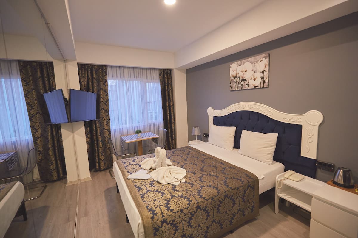 Ein Hotelzimmer mit einem großen Bett, einem Schreibtisch mit Stuhl, einem Flachbildfernseher und einem Fenster mit Vorhängen.