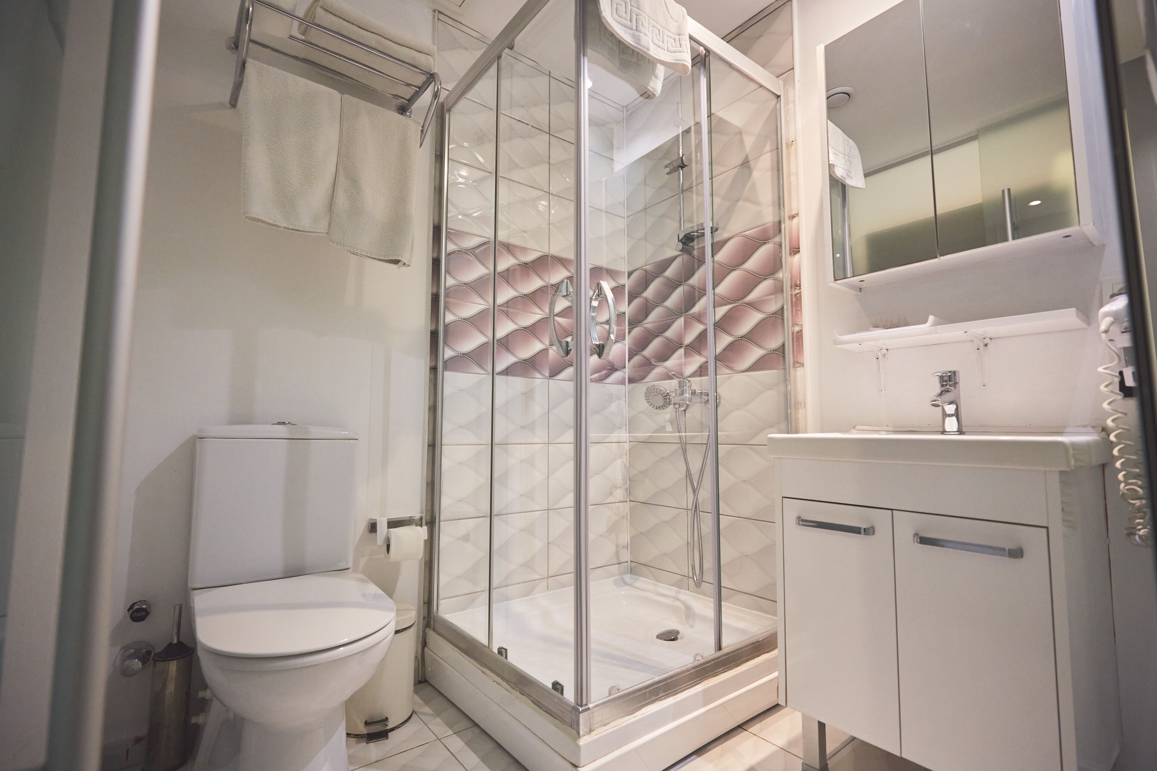 Un baño moderno con cabina de ducha de vidrio, inodoro y lavamanos con espejo.