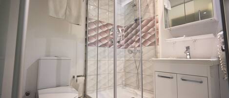 Un baño moderno con cabina de ducha de vidrio, inodoro y lavamanos con espejo.