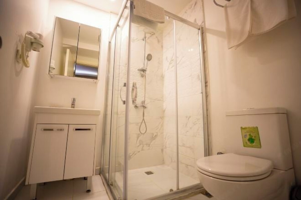 Une salle de bain avec une douche à parois de verre, des toilettes blanches, un lavabo avec un miroir et une serviette accrochée au mur.