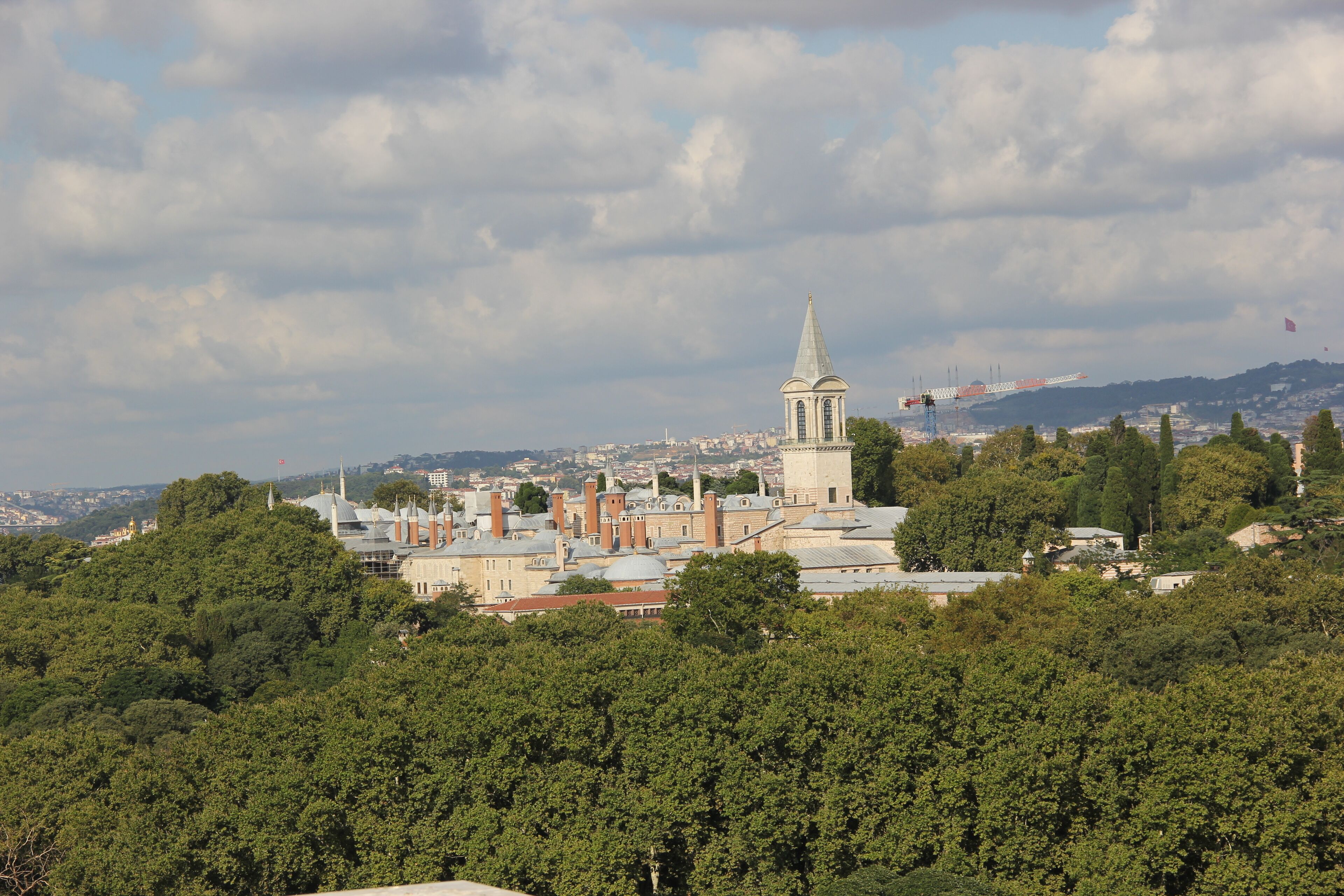 A historic building with a prominent tower, surrounded by dense greenery and a cityscape in the background.