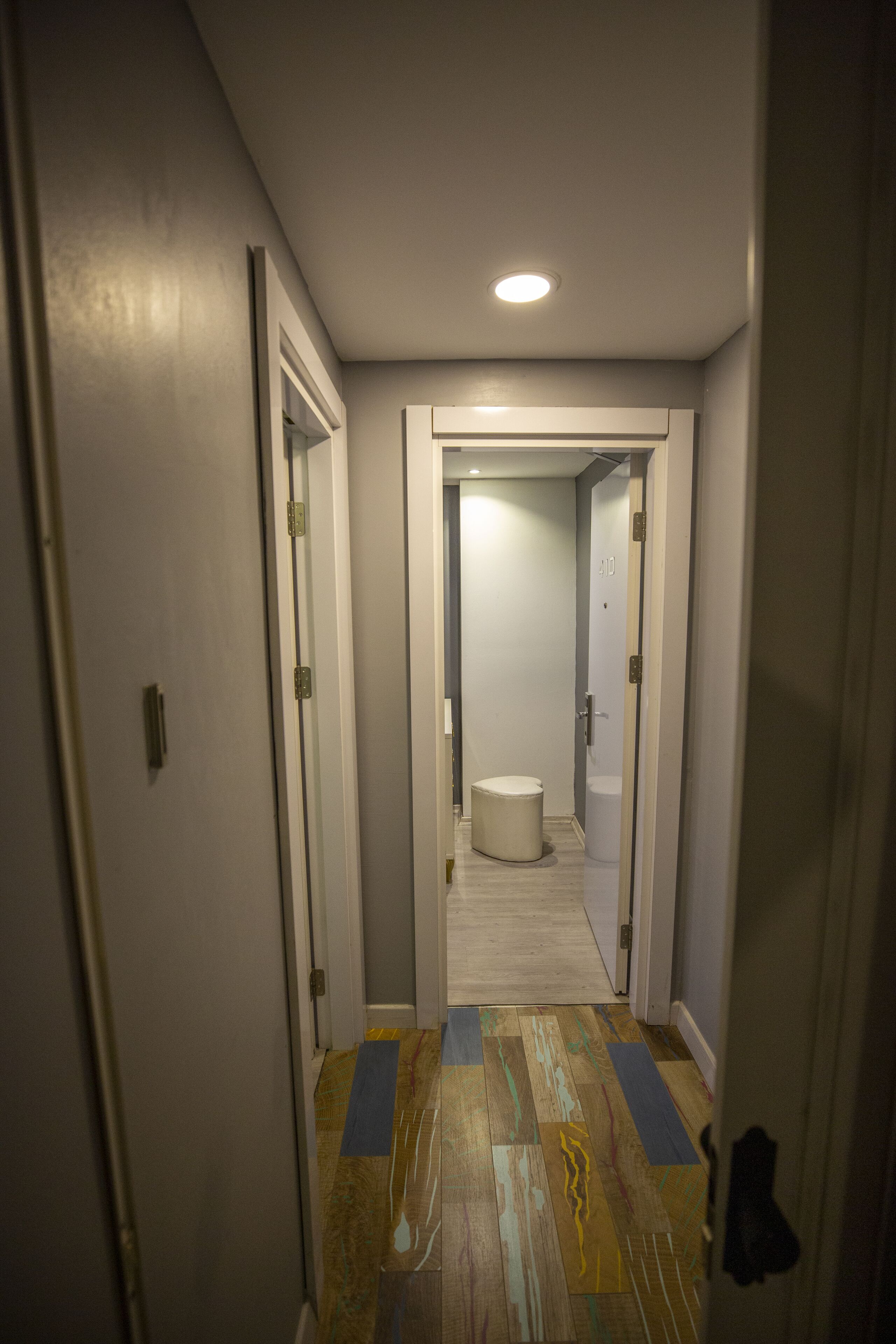 A narrow hallway with a wooden floor, white walls, and a ceiling light.