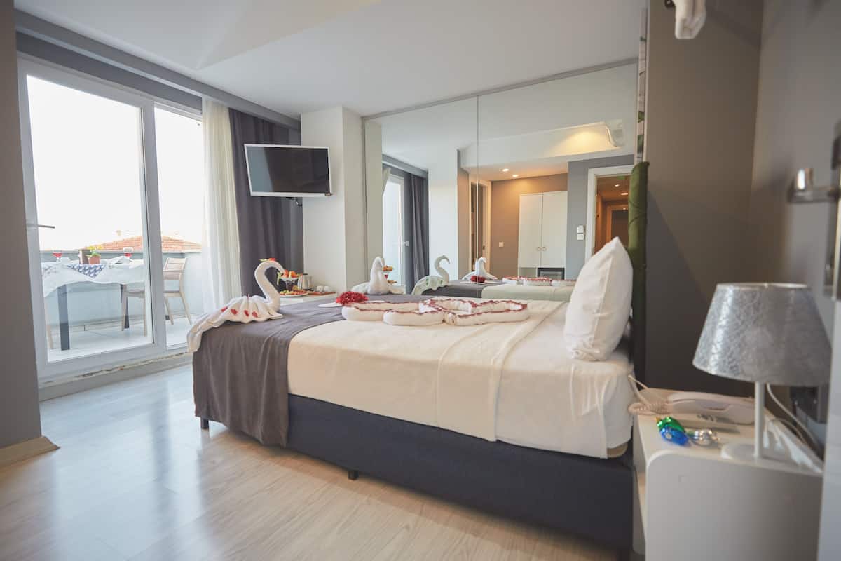 Ein Hotelzimmer mit einem großen Bett, einem Flachbildfernseher, einem Balkon mit Tisch und Stühlen und Blick auf die Stadt.