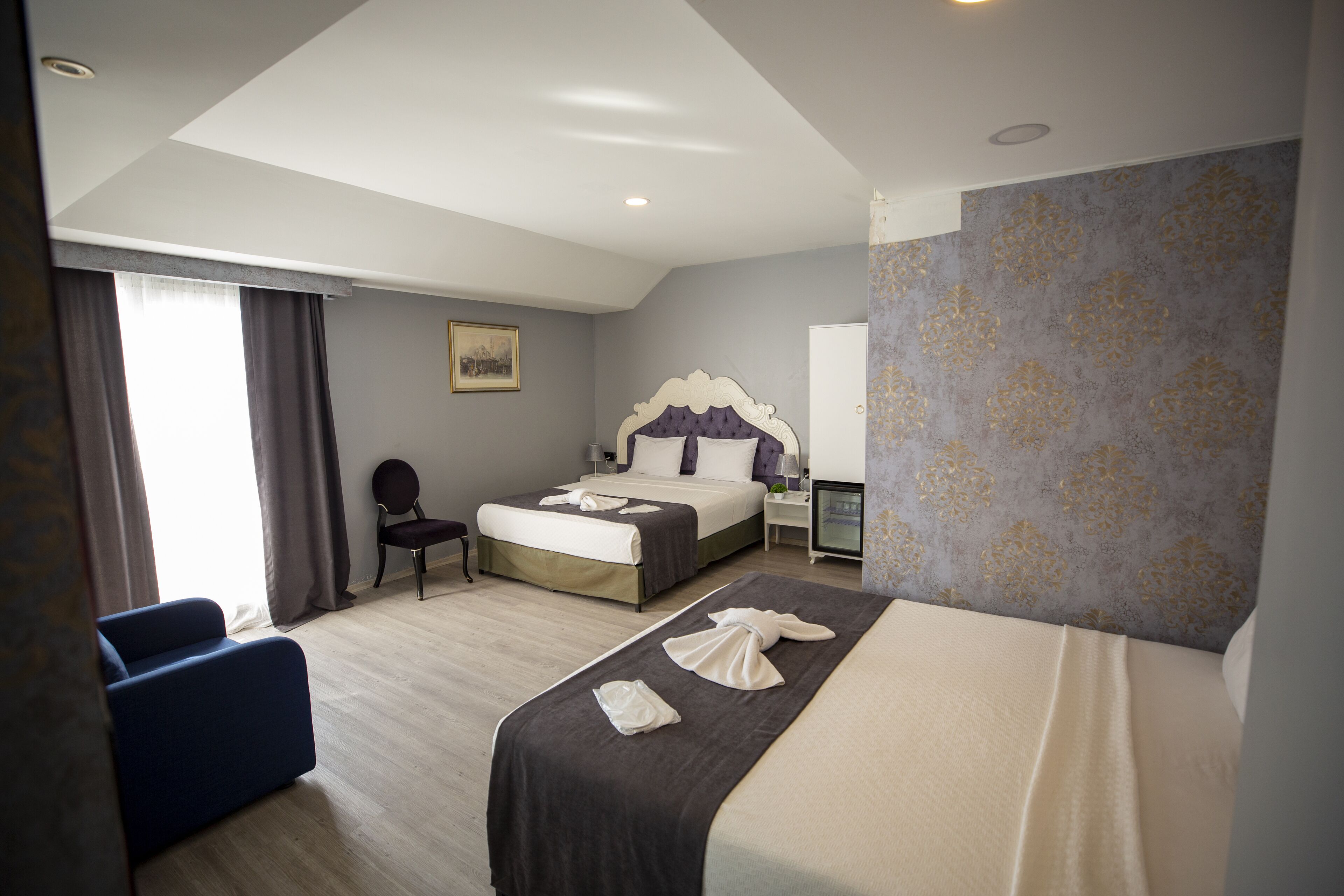 Ein Hotelzimmer mit zwei Betten, einem Schreibtisch, einem Stuhl und einem großen Fenster mit Vorhängen.