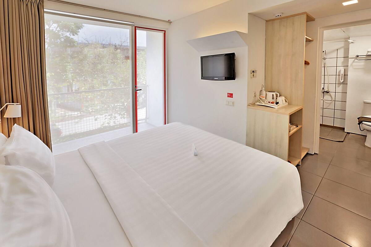 A hotel room with a large bed, a TV mounted on the wall, a small desk with a chair, and a shower area.