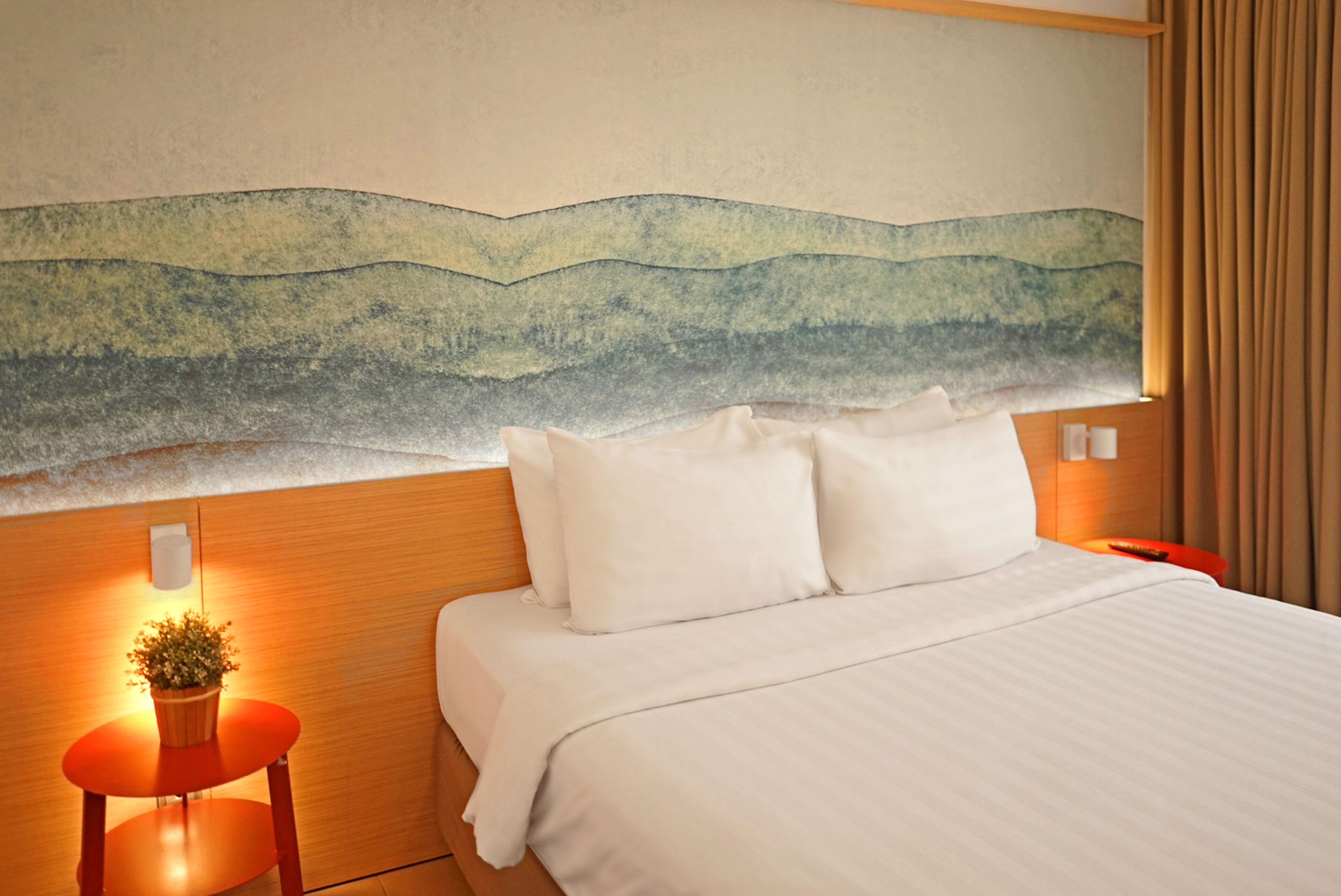 A hotel room with a bed, a nightstand with a lamp, and a wall-mounted painting.