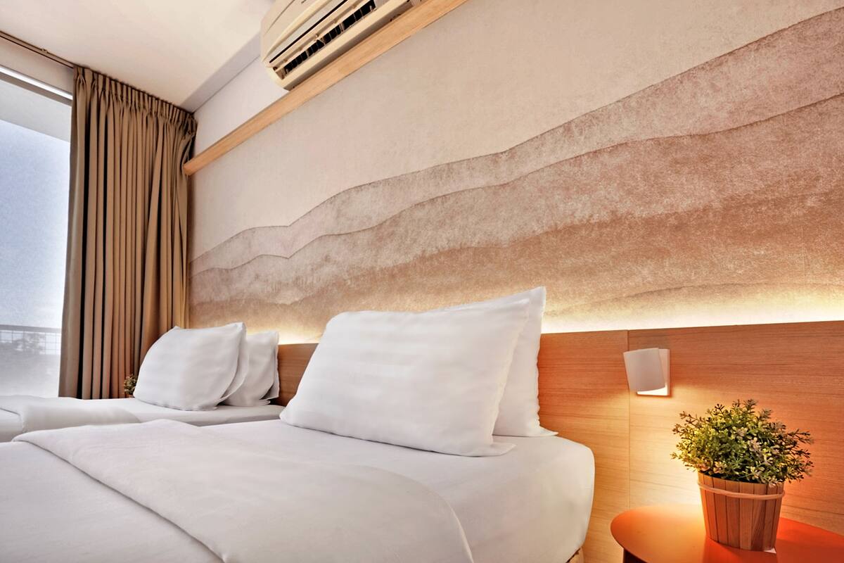 A hotel room with two beds, a wooden headboard, a potted plant, and a window with curtains.