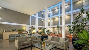 Eine geräumige Lobby mit hoher Decke, mehreren Sitzbereichen und vielfältigen Pflanzen.