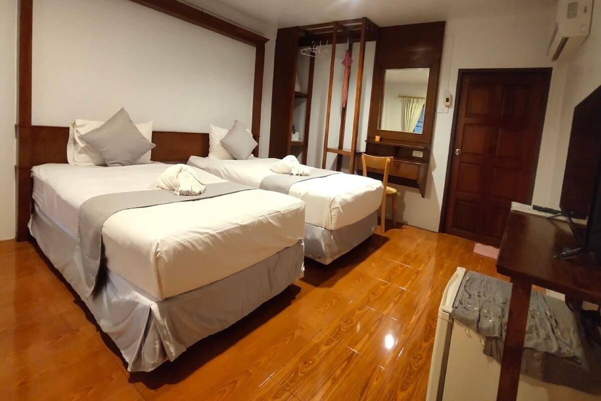 Habitación de hotel con dos camas, piso de madera, escritorio con silla, espejo y televisor.