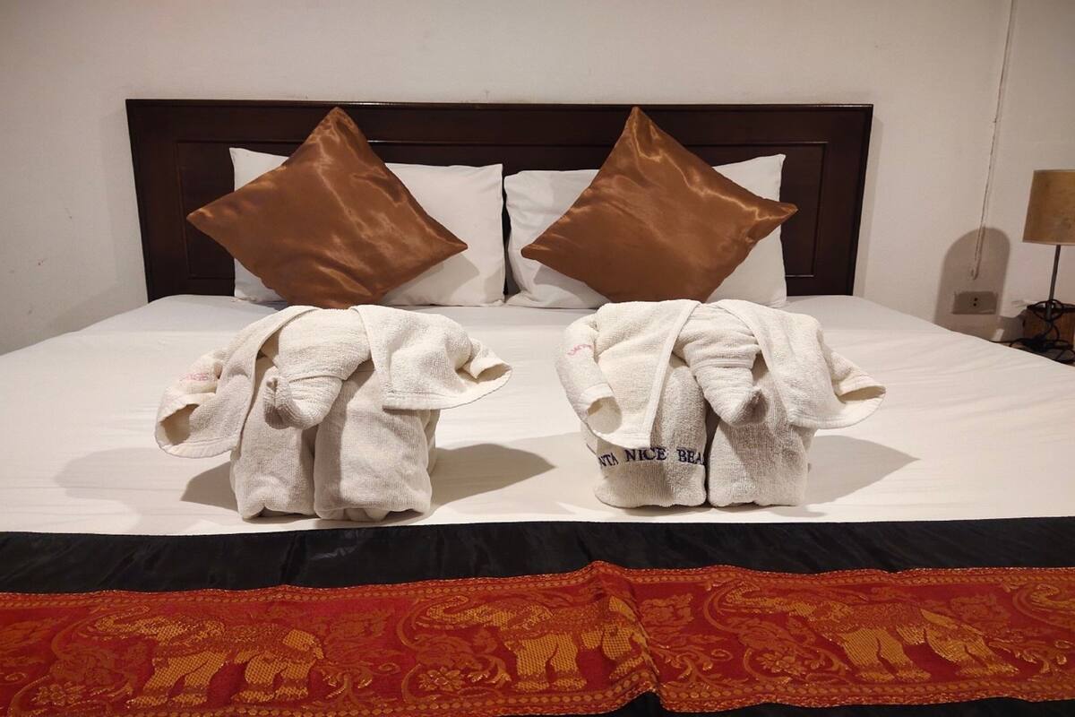 Habitación de hotel con una cama grande, dos almohadas marrones y dos toallas con forma de elefantes.