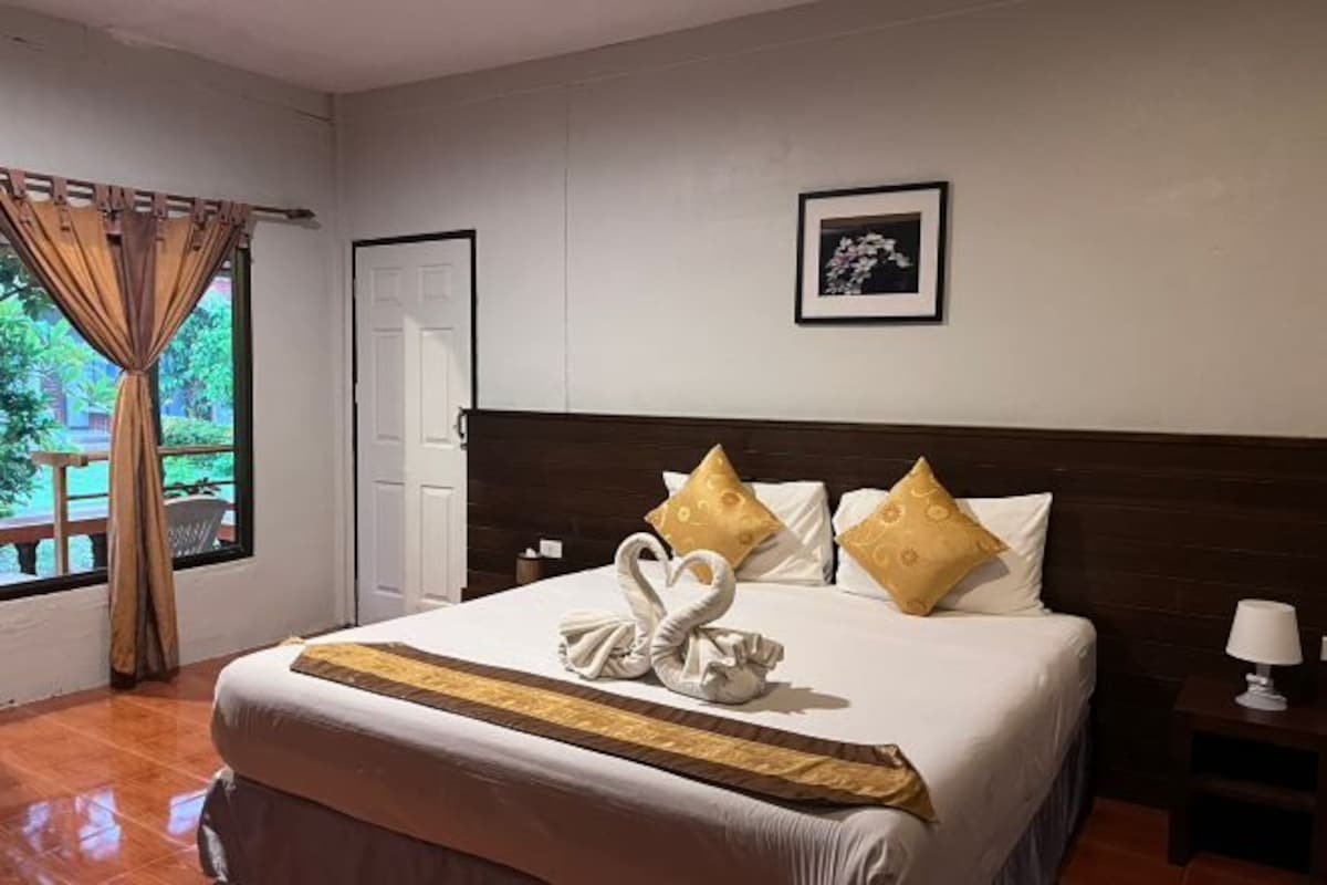 A hotel room with a large bed, a wooden headboard, a framed picture on the wall, and a window with curtains.