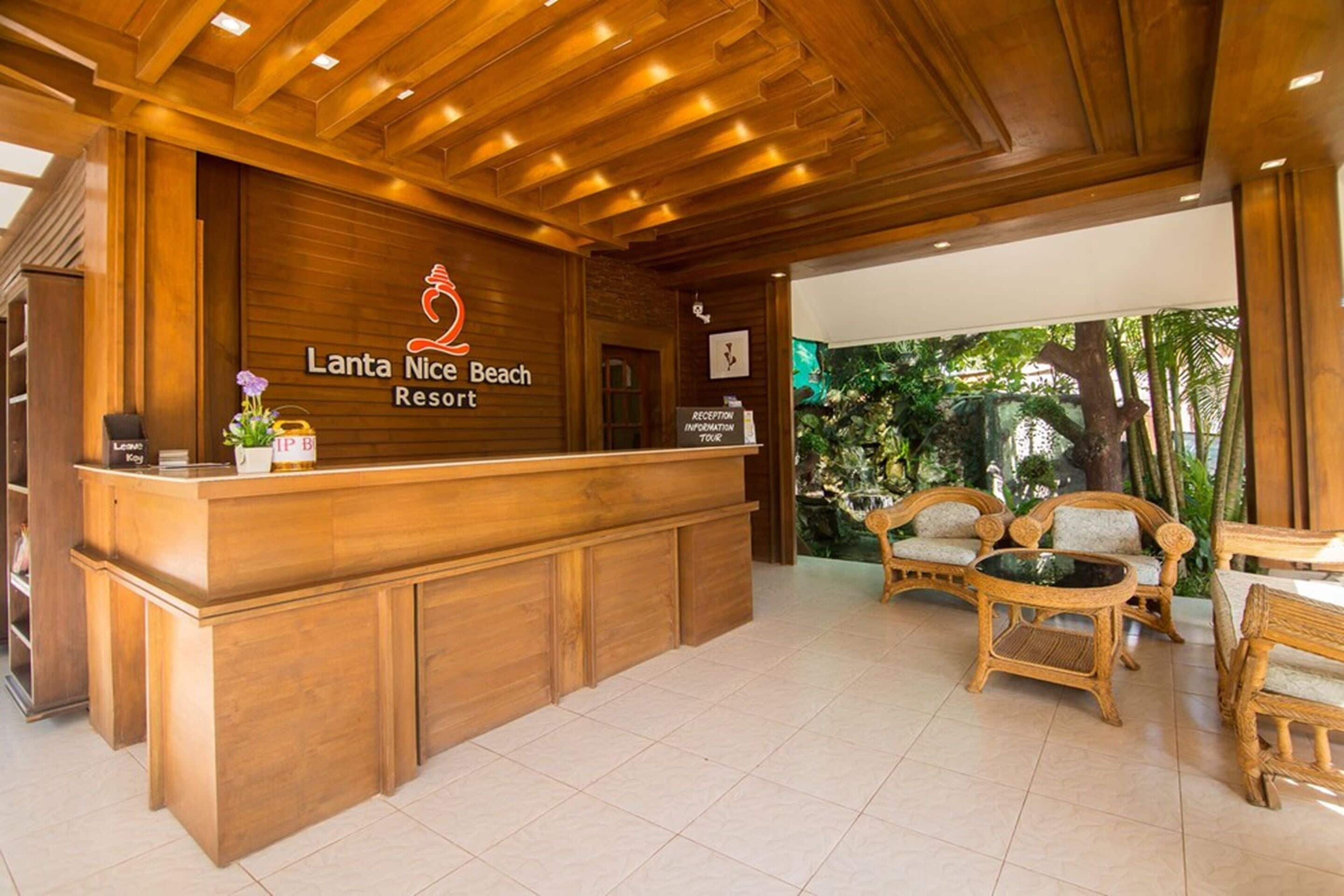 A reception desk at Lanta Nice Beach Resort with a wooden design, a reception information sign, and wicker furniture.