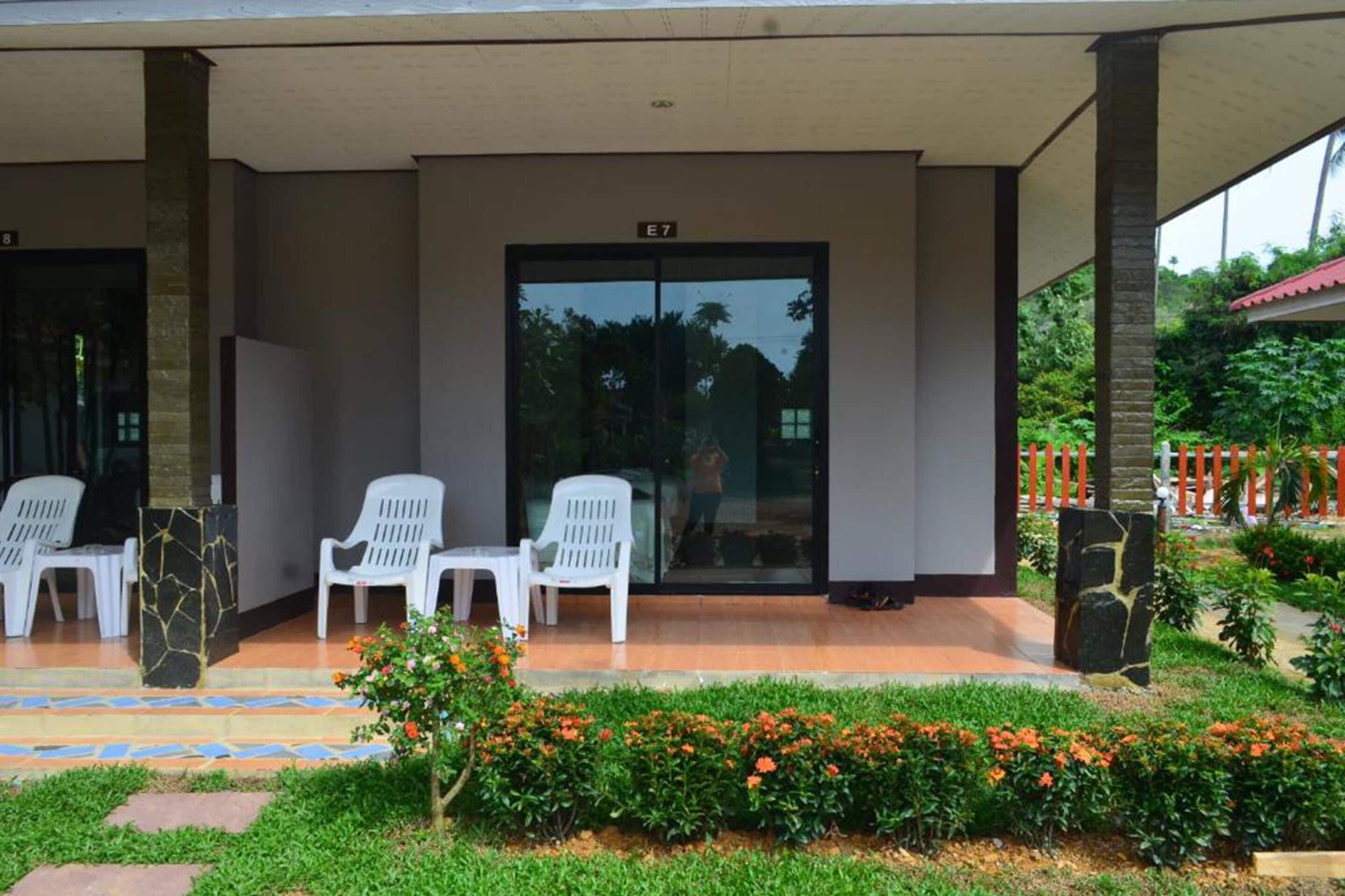 A covered outdoor area with white plastic chairs and a glass door marked E7.