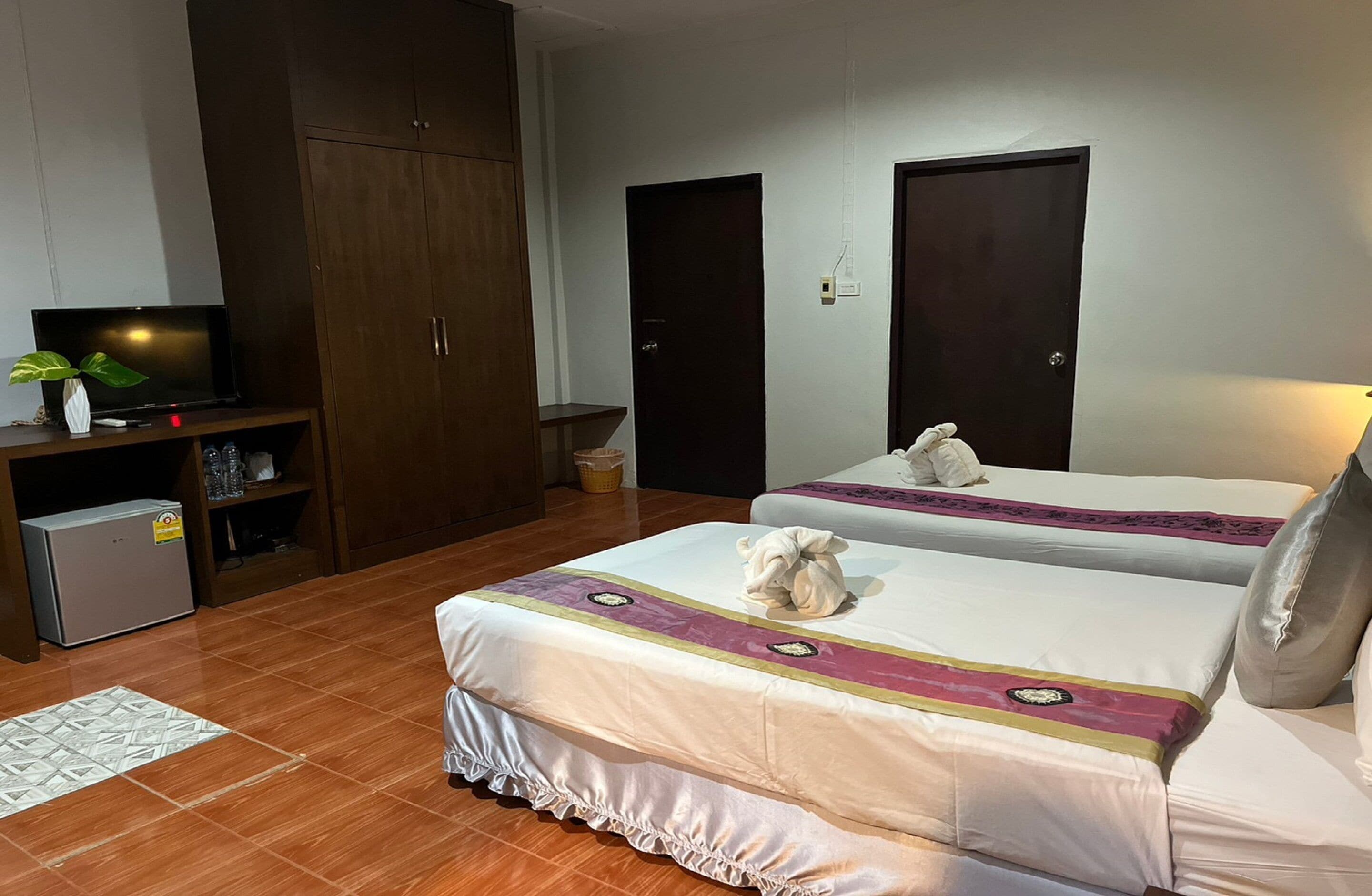 A hotel room with two beds, a TV, a wardrobe, and a small fridge.