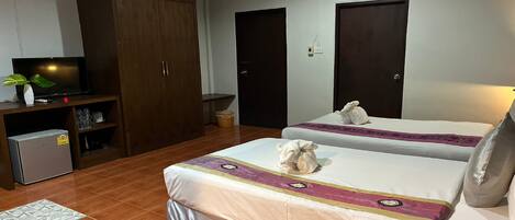 A hotel room with two beds, a TV, a wardrobe, and a small fridge.