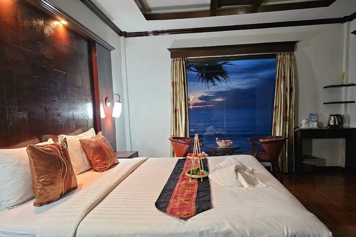 Habitación de hotel con una cama grande, una mesita de noche, un escritorio y vistas al océano.