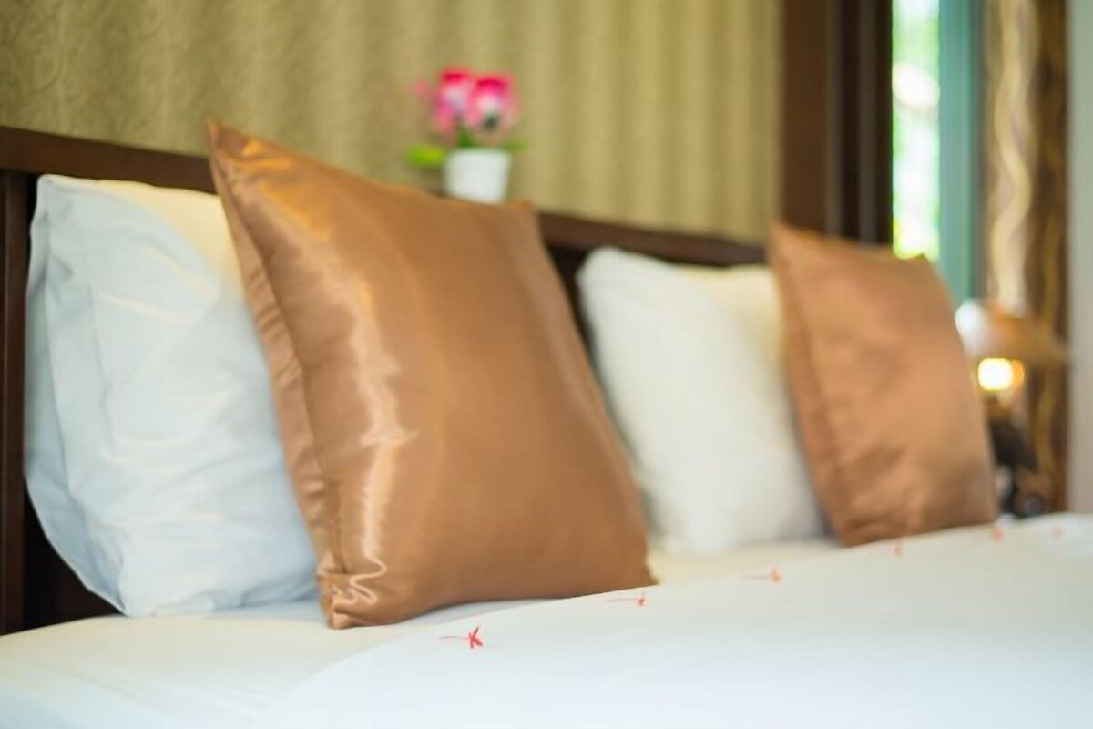 A bed with three pillows and a floral decoration in the background.