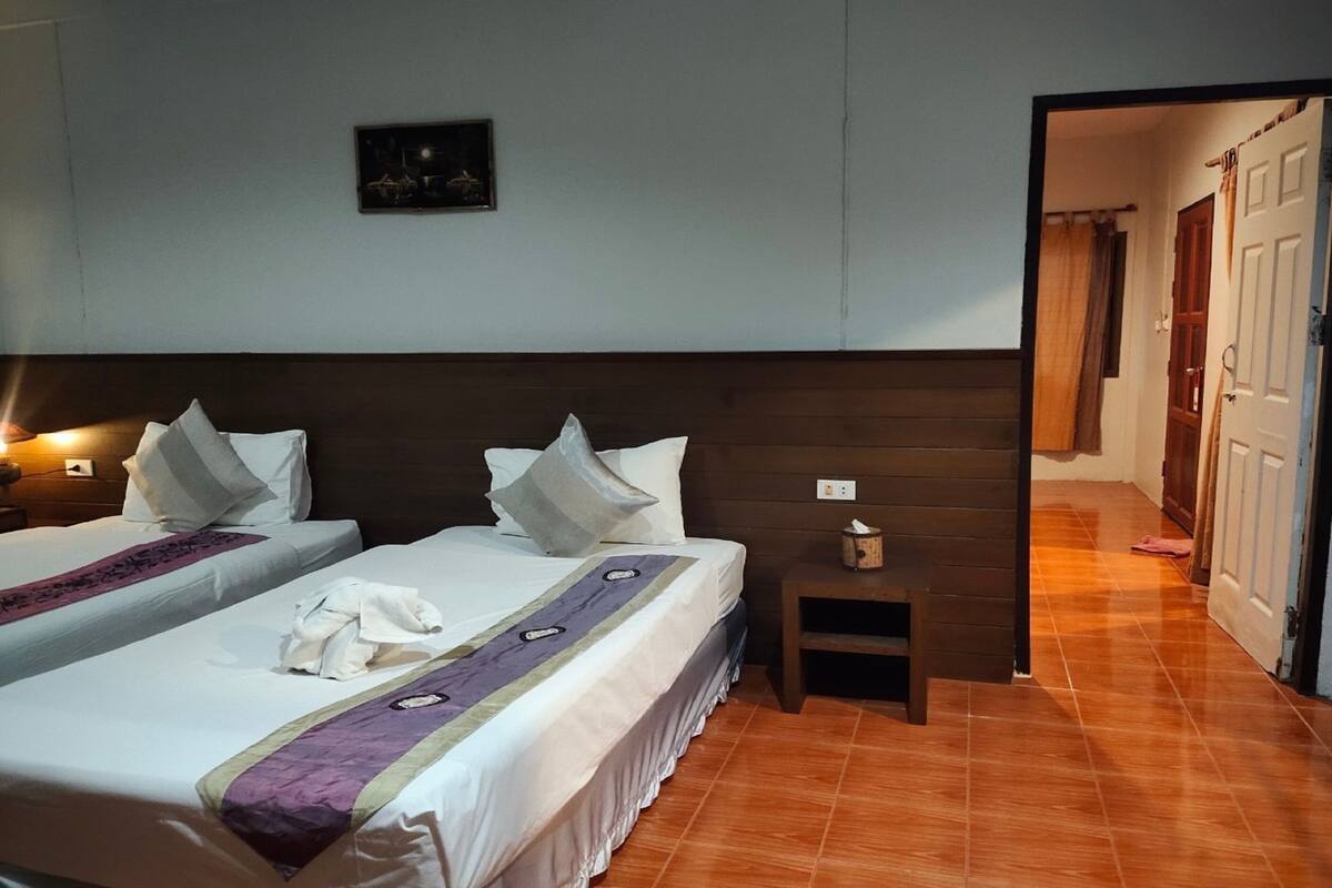 Habitación de hotel con dos camas, una mesita de noche, un cuadro en la pared y suelo de baldosas.