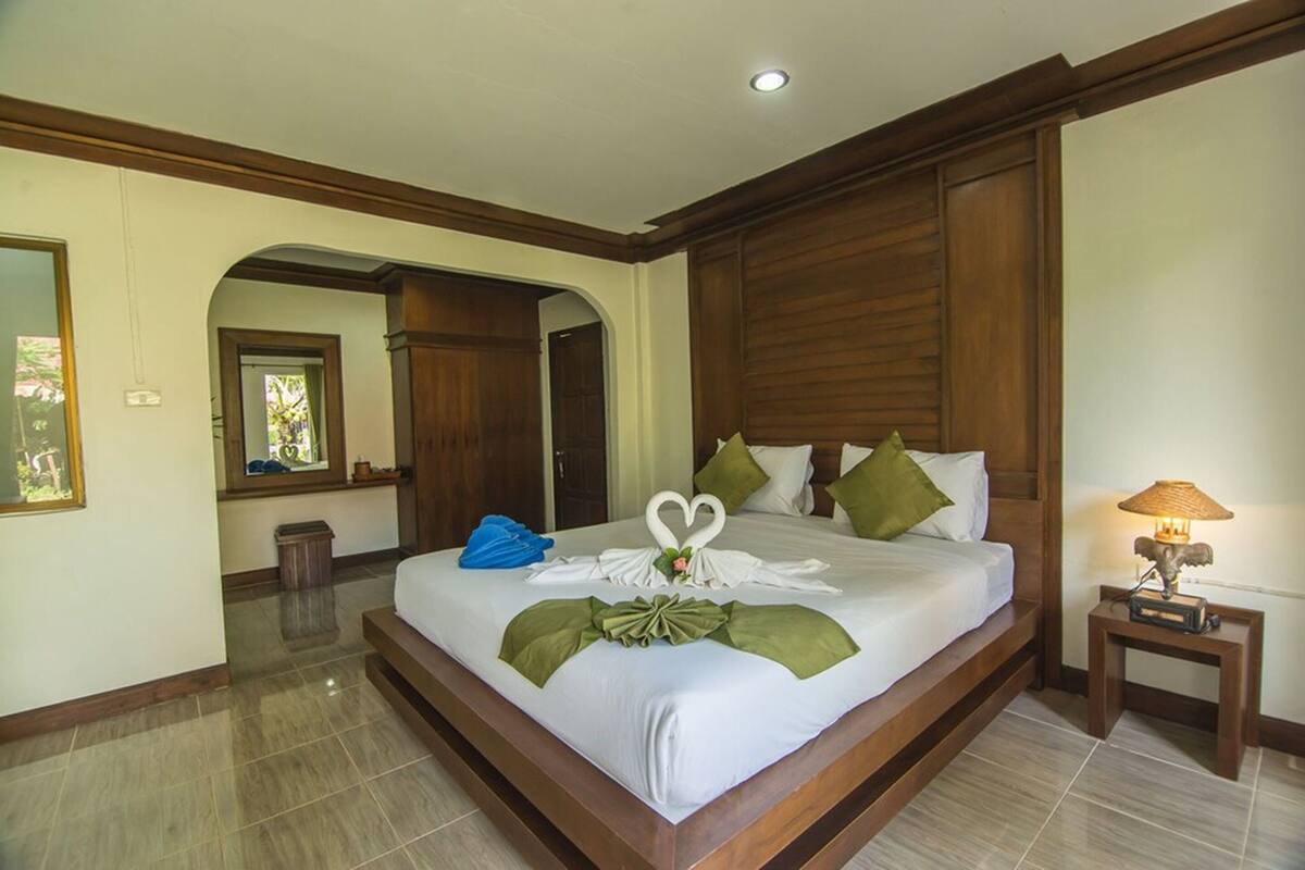 Un dormitorio amplio y elegante con cabecera de madera, cama bien tendida y mesita de noche con lámpara.