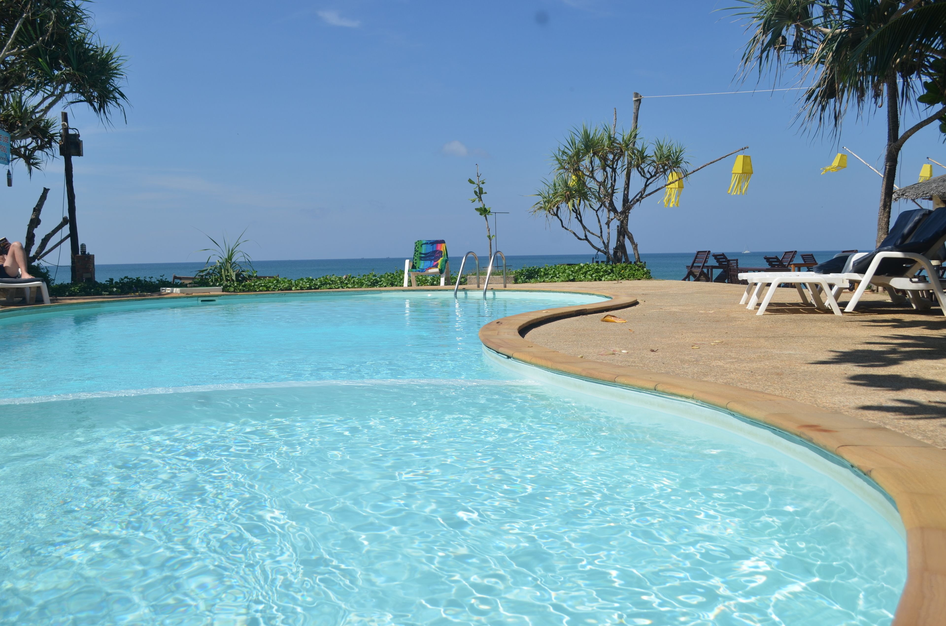 A pool with clear water, surrounded by lounge chairs and umbrellas, with a view of the ocean.