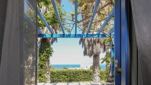 Un balcón con vista al mar, una mesa con una planta y un sombrero, y dos sillas de mimbre.