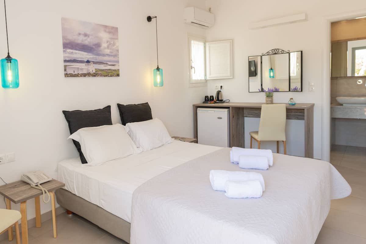 A neatly arranged hotel room with a bed, bedside table, desk, and a small kitchenette.