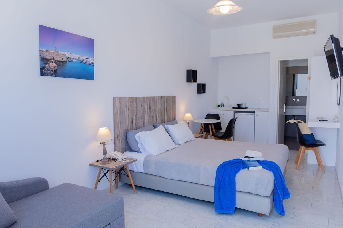 A modern hotel room with a bed, bedside table, lamp, and a painting of a coastal scene.