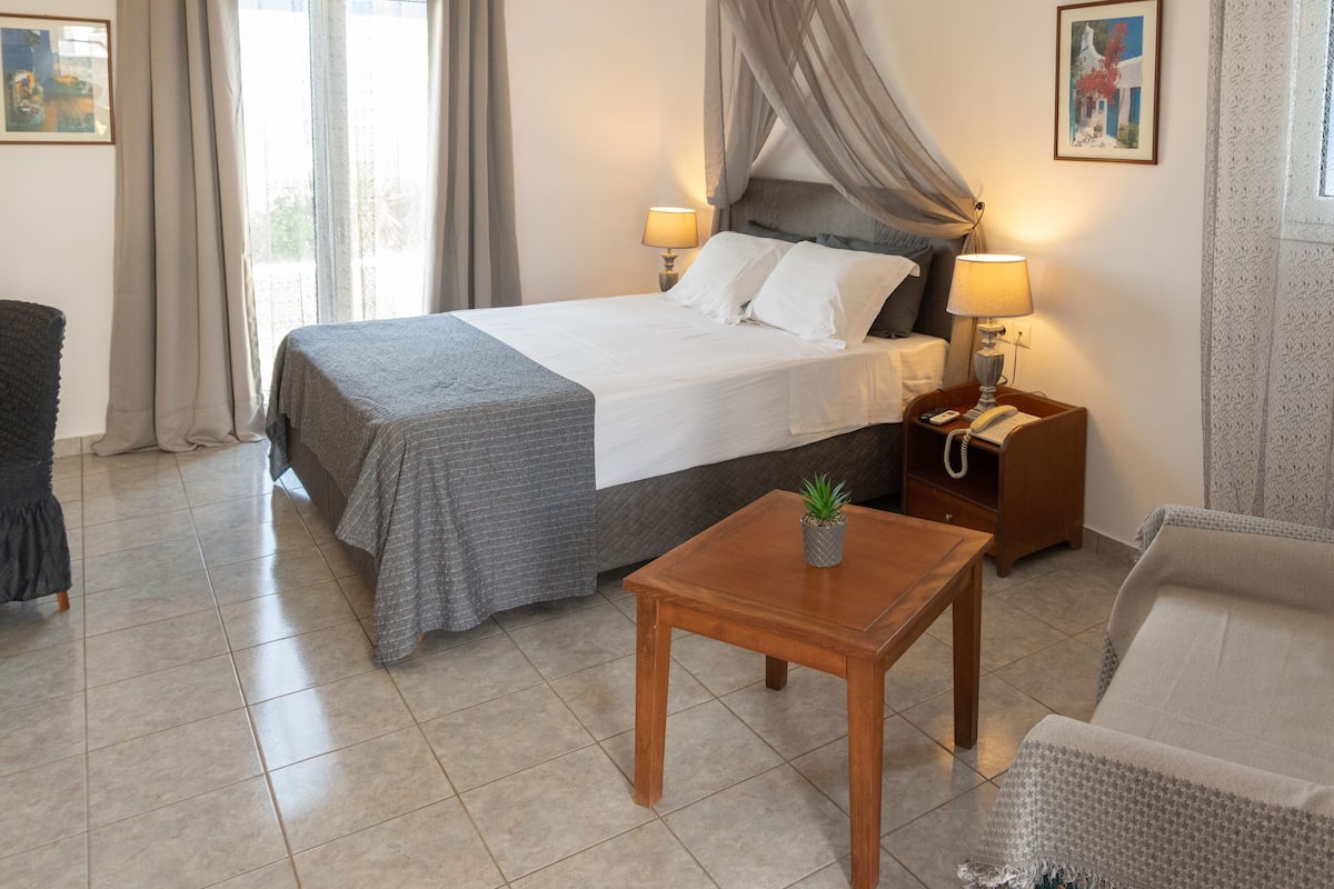 A hotel room with a bed, bedside lamps, a small table with a plant, a chair, and a picture on the wall.