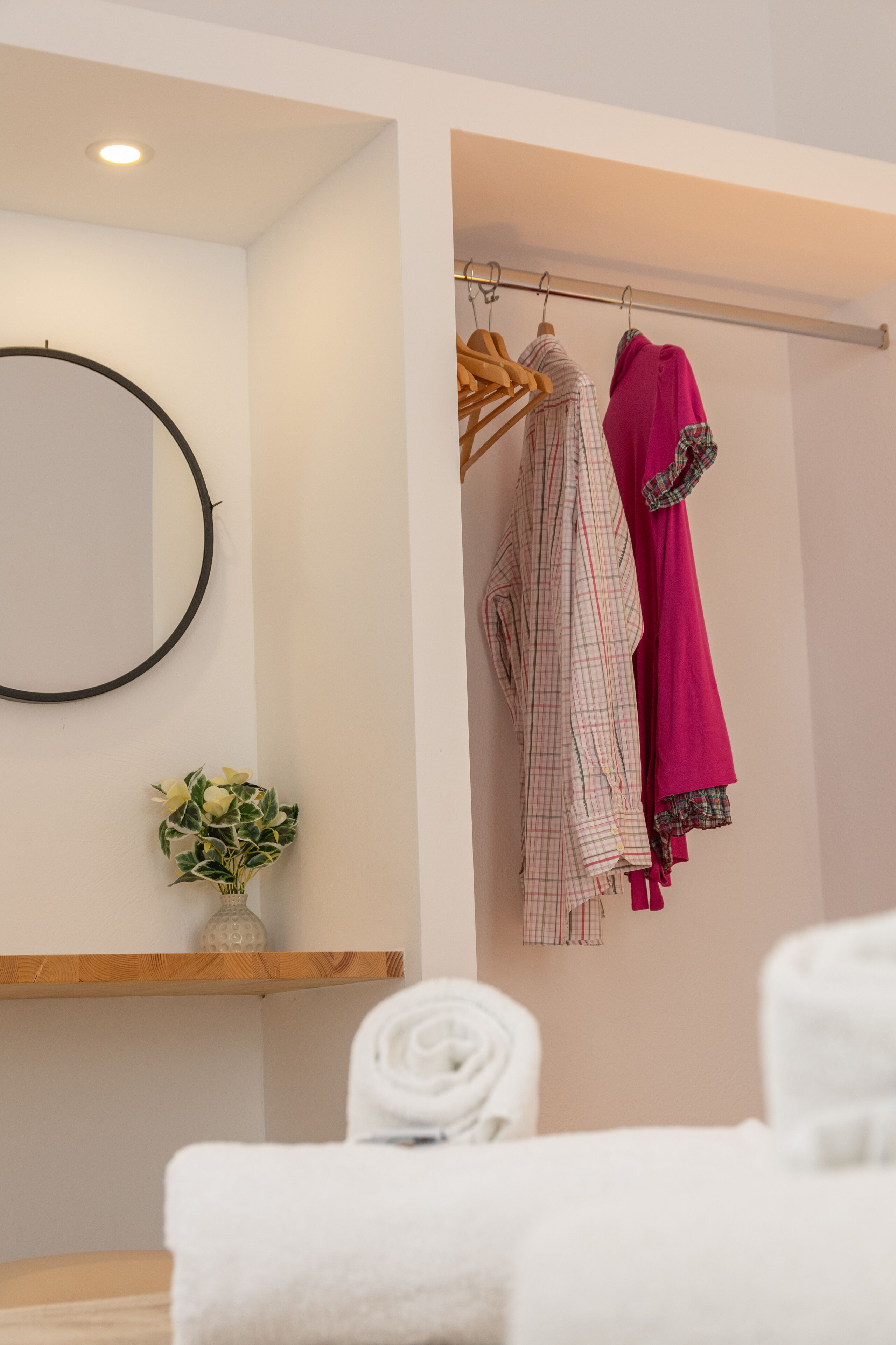 A bathroom with a wooden shelf, a mirror, and a towel rack with folded towels and clothes.