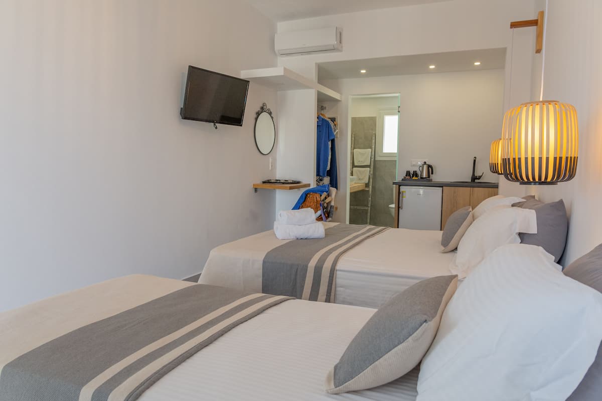 A hotel room with two beds, a TV mounted on the wall, a bathroom visible through an open door, and a hanging lamp.