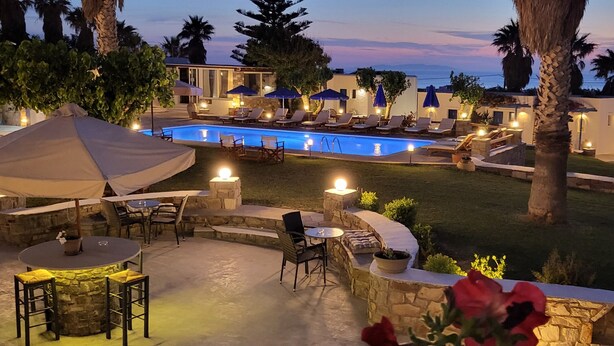 Un área junto a la piscina con sillones de descanso, una mesa y sombrillas.