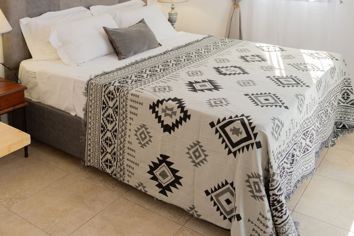 A neatly arranged bedroom with a bed, bedside lamps, and a patterned bedspread.