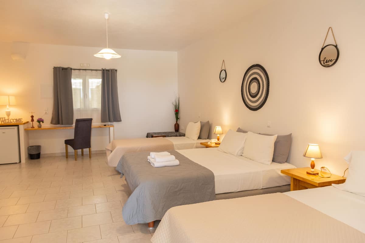A hotel room with two single beds, a desk, a chair, a small table with a lamp, and a wall-mounted target decoration.