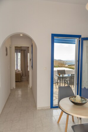 A hallway leading to a balcony with a table and chairs, and a bed in the background. - Fragoulis Village (Paros)