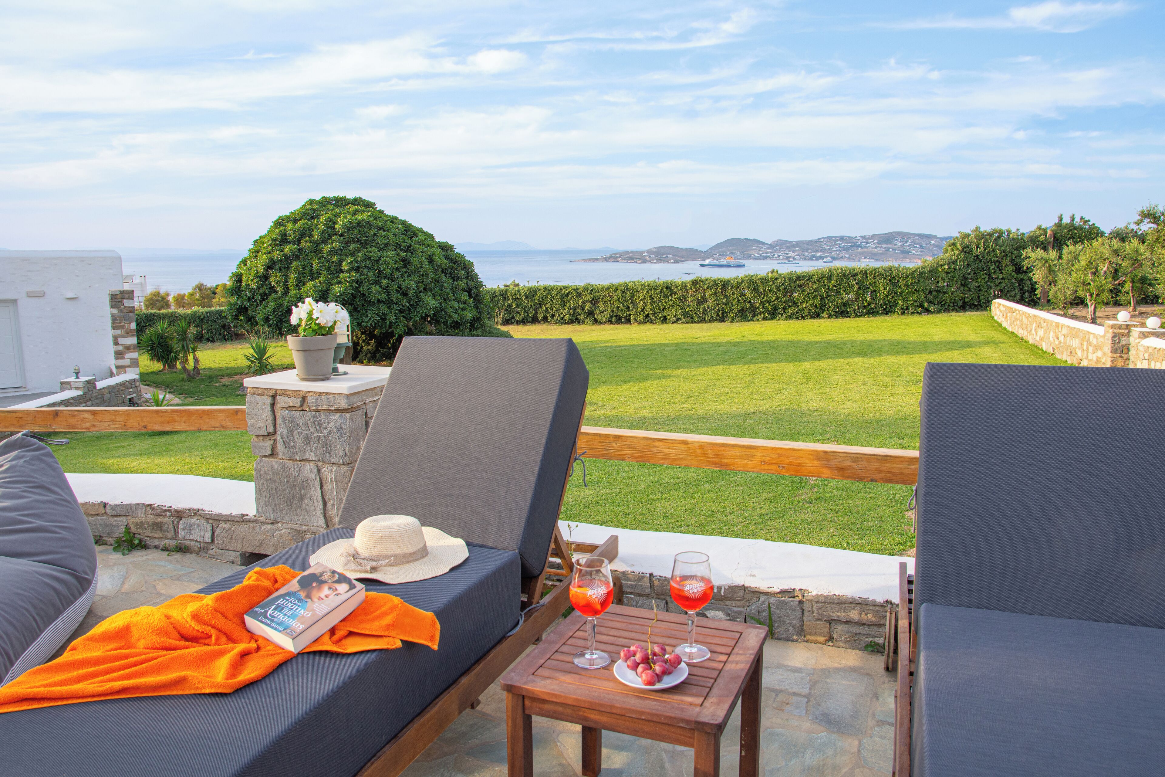 Eine Terrasse mit zwei Loungestühlen, einem Tisch mit Getränken und einem Buch, und Blick auf Meer und Grün.