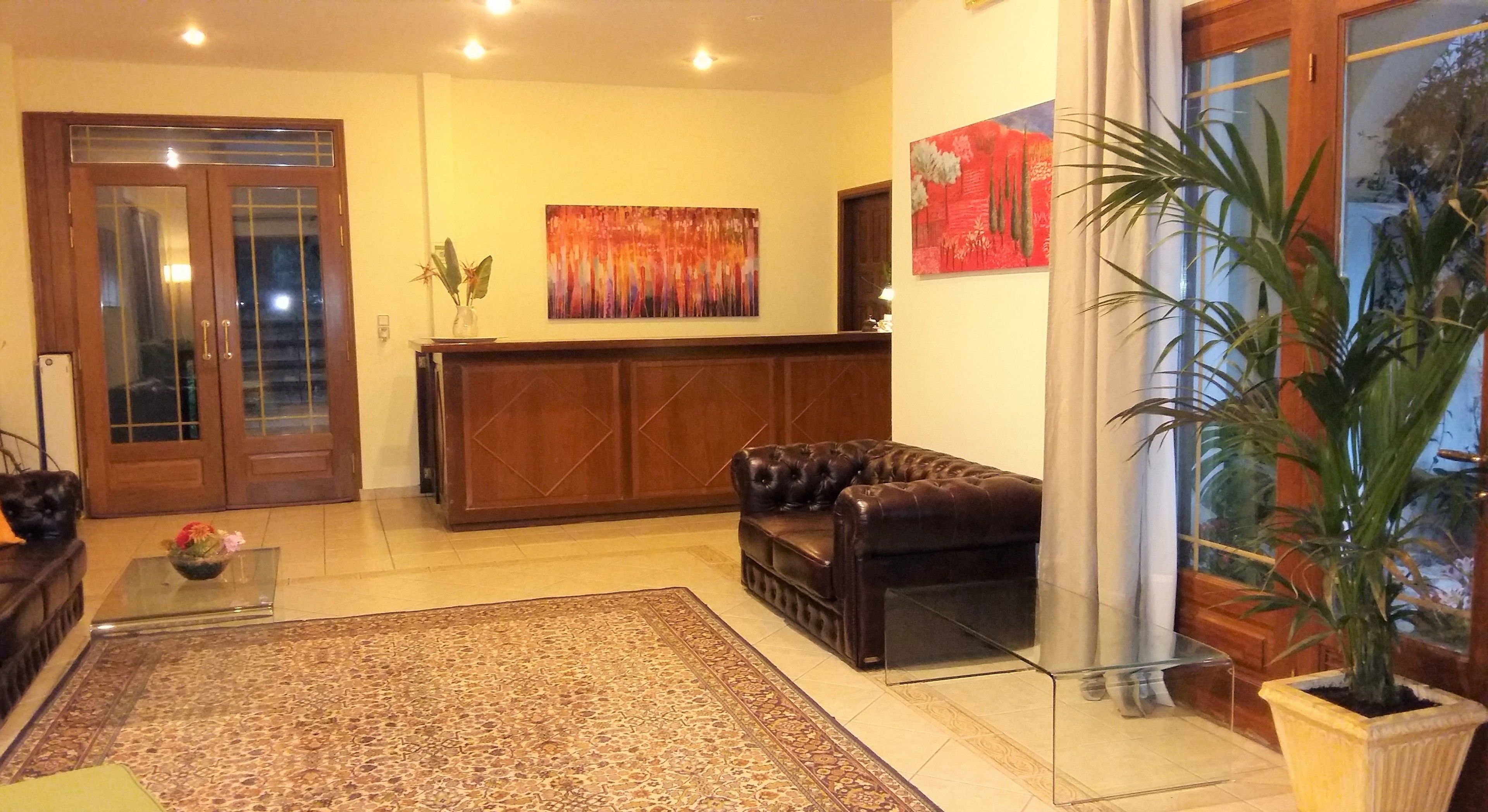 A lobby with a reception desk, a leather sofa, a patterned rug, and a large potted plant.