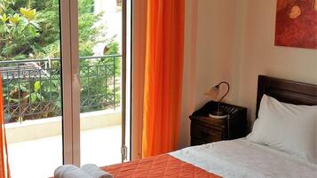 A hotel room with a bed, a nightstand, a lamp, a painting, and a view of greenery outside.